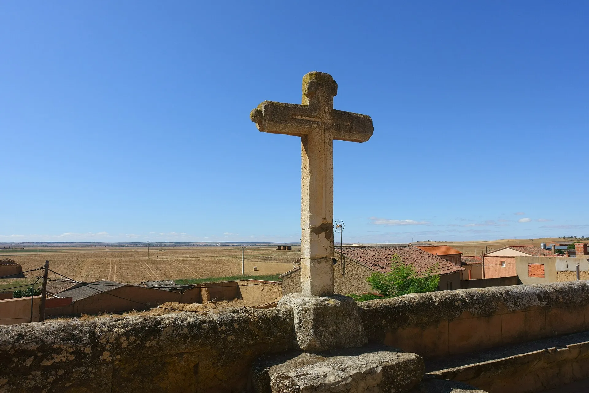 Cruz de piedra sobre los tejados de Prado con la llanura de cereal hasta el horizonte