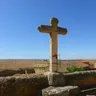 Cruz de piedra sobre los tejados de Prado con la llanura de cereal hasta el horizonte