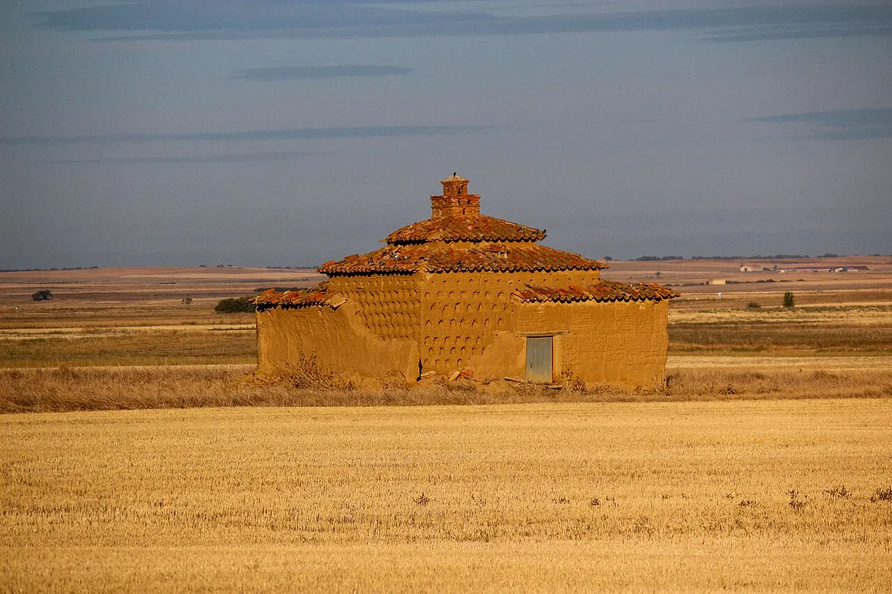 Palomar de adobe en un campo de cereal segado bajo un cielo amplio, cerca de Tapioles