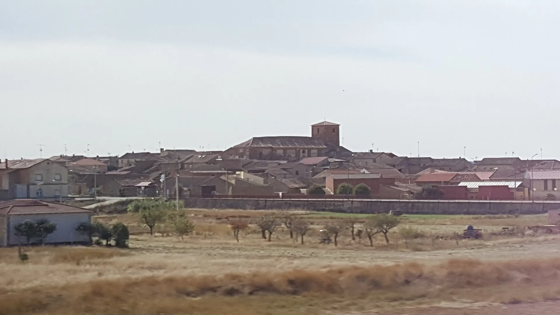 Vista de Cerecinos de Campos con la torre de la iglesia sobre los tejados y campos secos delante
