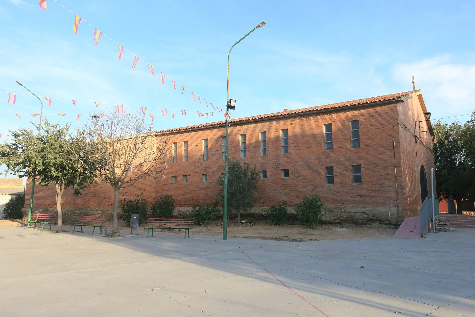 Iglesia de ladrillo de Nuestra Señora de los Rayos en Tapioles, frente a una plaza con bancos