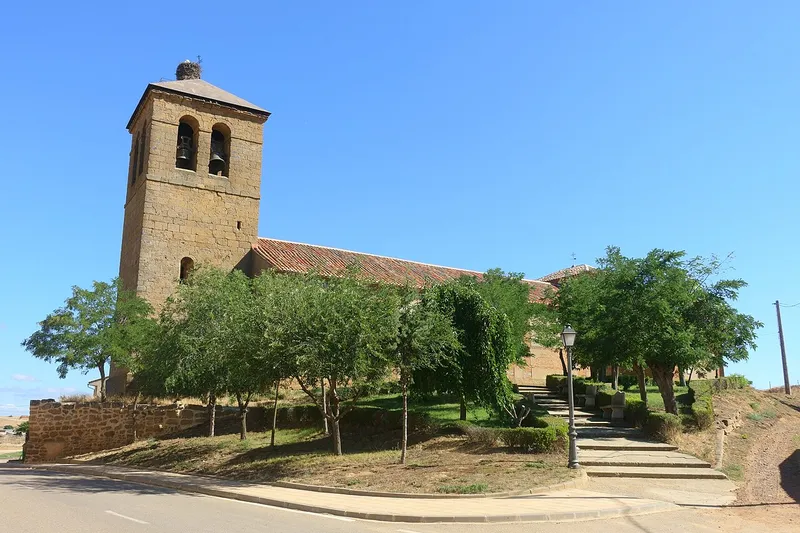 Torre de piedra de la iglesia de San Pedro de Villalobos entre árboles, con escalinata