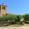 Torre de piedra de la iglesia de San Pedro de Villalobos entre árboles, con escalinata